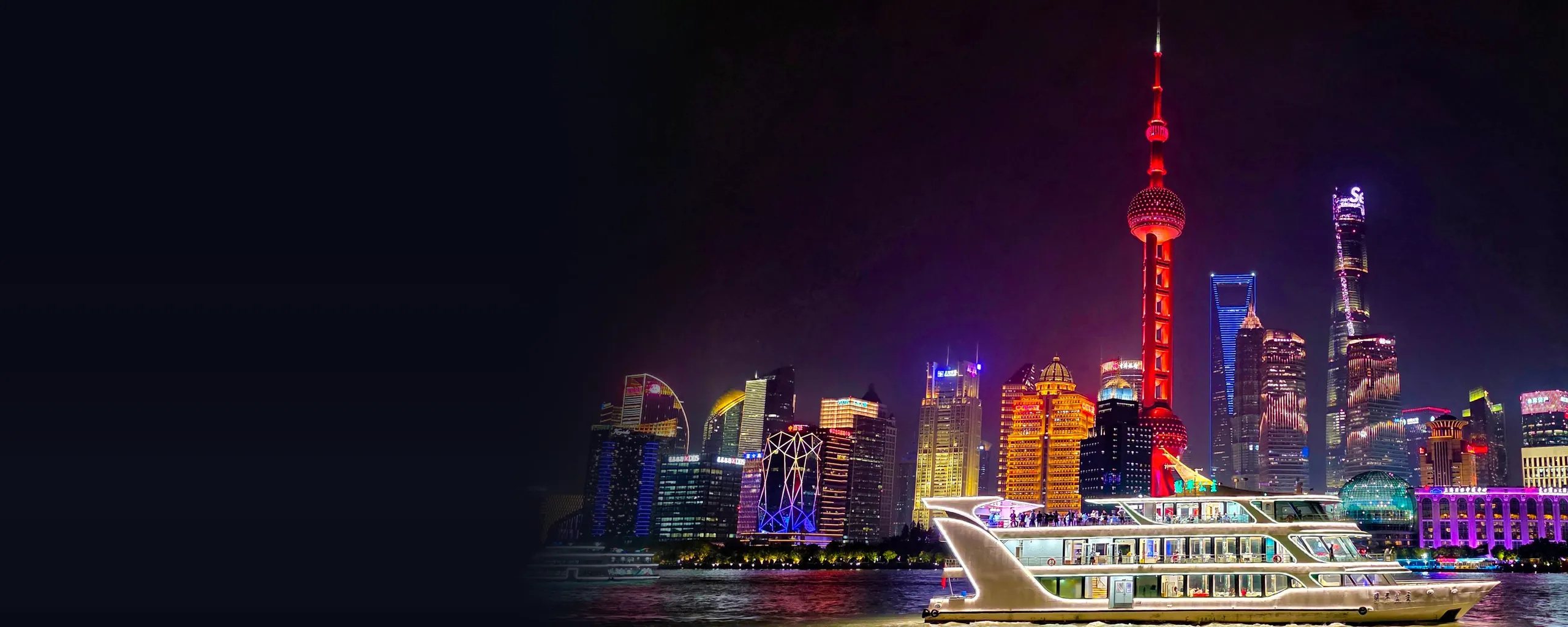 A lit-up cruise boat on the Huangpu River at night, with the red Oriental Pearl Tower and the glowing towers of Pudong rising behind it