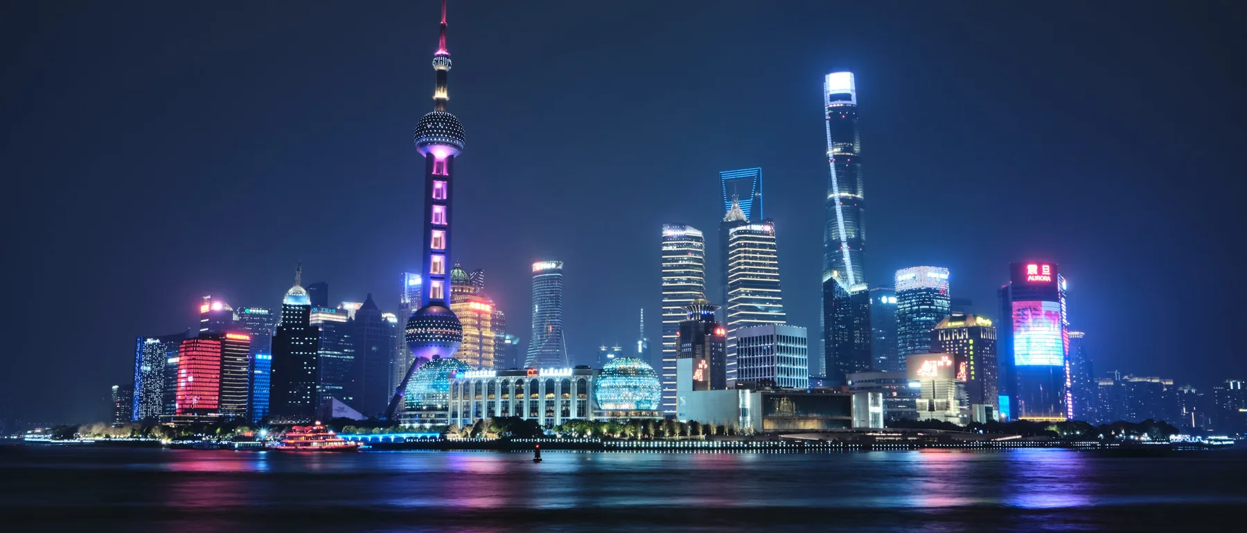 Pudong's skyline across the Huangpu at night, with the Oriental Pearl Tower and glass towers reflected in the water
